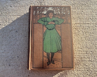 May include: Antique book with a brown cover and a detailed illustration. The illustration features a woman in a green dress, standing in front of a tree. The book's cover has a decorative border.