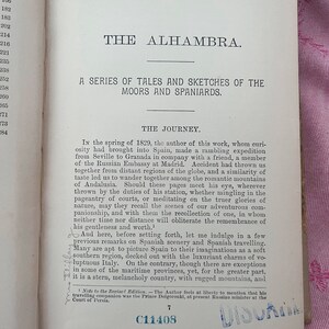 May include: Open book page with text titled "THE ALHAMBRA" and "A SERIES OF TALES AND SKETCHES OF THE MOORS AND SPANIARDS." The page has a list of numbers on the left and a stamp that says "PUBLIC LIBRARY BINGHAMTON, N.Y."