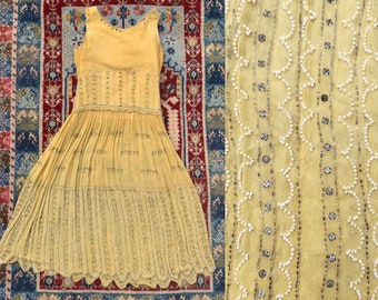 May include: A vintage yellow dress with a sleeveless design and a pleated skirt. The dress is adorned with intricate beadwork and decorative embellishments. The dress is likely made of a lightweight fabric, perfect for warmer weather.