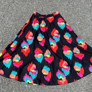 May include: A black, flared skirt with a vibrant, colorful pattern. The design features repeating, abstract shapes in shades of red, orange, turquoise, yellow, and pink. The skirt is made of a lightweight fabric.