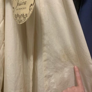 Puede incluir: Tela de color crema con una etiqueta que dice "by Jessica San Francisco". La tela parece ser un material natural, posiblemente lino o algod&oacute;n, con textura visible y algo de decoloraci&oacute;n. La etiqueta tiene un dise&ntilde;o ornamentado.