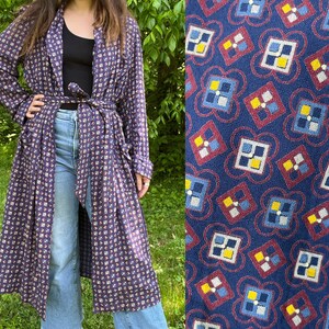 May include: A long, navy blue robe with a repeating geometric pattern in red, yellow, and white. The robe is tied at the waist with a matching belt. The fabric appears to be lightweight, suitable for warmer weather.