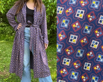 May include: A long, navy blue robe with a repeating geometric pattern in red, yellow, and white. The robe is tied at the waist with a matching belt. The fabric appears to be lightweight, suitable for warmer weather.