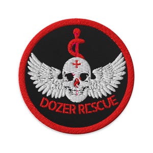 Puede incluir: Parche bordado con fondo negro y borde rojo. El parche presenta una calavera blanca con alas, una cruz roja y las palabras "DOZER RESCUE" en rojo.