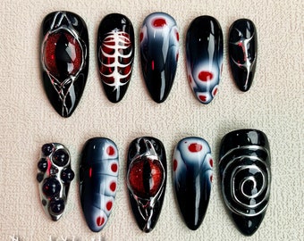 May include: Ten black and white nail art designs with red accents. The designs include an eye, a ribcage, a swirl, and a cluster of black beads.
