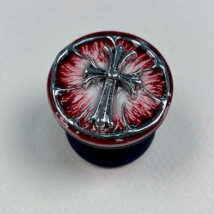 May include: A circular phone grip featuring a metallic silver cross emblem centered on a glossy red and white marbled background. The design is encased in a silver frame with a segmented circular border, mounted on a solid black circular base.