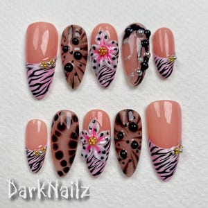 May include: Set of ten false nails with a pink and black zebra print design, black and brown leopard print design, and a pink flower design. Some nails have black and silver beads.
