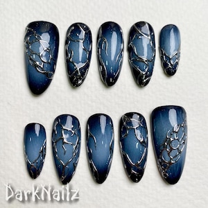 Puede incluir: Diez uñas postizas azules y plateadas con un efecto degradado azul oscuro y diseños de lámina plateada. Las uñas están dispuestas en dos filas de cinco.