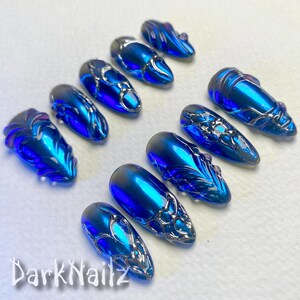 Pu&ograve; includere: Set di dieci unghie finte blu e argento con un design a spirale. Le unghie sono lunghe e di forma ovale.