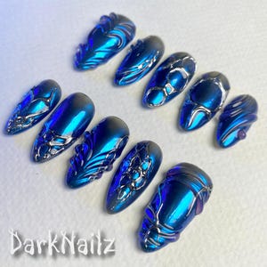 Pu&ograve; includere: Set di dieci unghie finte blu e argento con disegni intricati. Le unghie sono di forma ovale e hanno una finitura lucida.