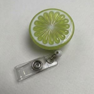 May include: A lime slice badge reel with a clear plastic clip and a retractable cord. The lime slice is green with white accents, resembling a real lime. The badge reel is a fun and functional accessory.