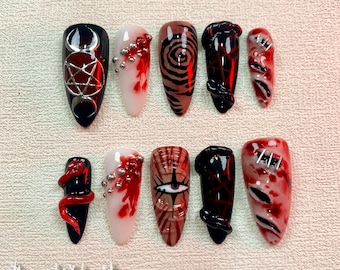 Puede incluir: Conjunto de diez uñas postizas con diferentes diseños. Los diseños incluyen un pentagrama, una espiral, una serpiente, un ojo sangrante y una herida cosida. Las uñas están pintadas de negro, rojo y blanco.
