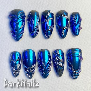 Pu&ograve; includere: Dieci unghie finte blu e argento con diversi design. Le unghie hanno una finitura metallica e sono decorate con linee e vortici argentati.