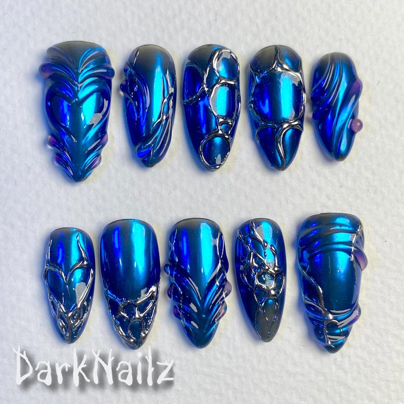 Pu&ograve; includere: Dieci unghie finte blu e argento con diversi design. Le unghie hanno una finitura metallica e sono decorate con linee e vortici argentati.