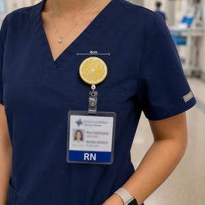 May include: A yellow and white lemon slice badge reel, approximately 1.5 inches in diameter, attached to a clear plastic ID holder. The ID holder displays the text "RN" and a medical center logo. The person is wearing a navy blue scrub top.