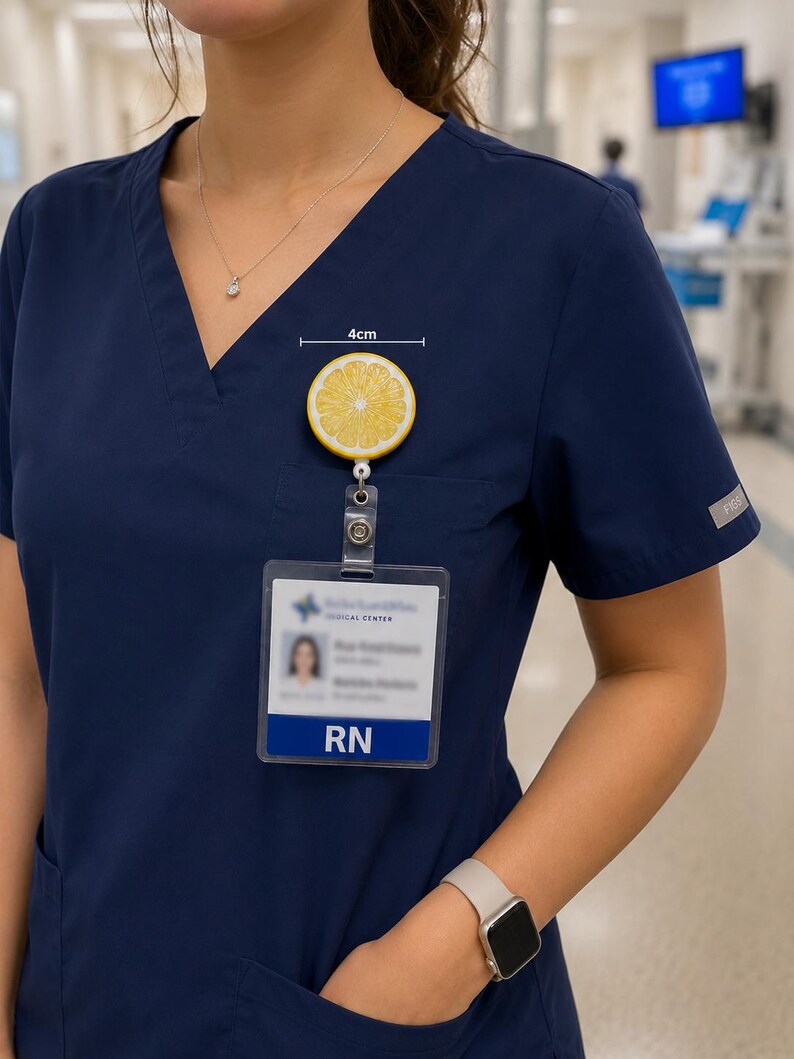 May include: A yellow and white lemon slice badge reel, approximately 1.5 inches in diameter, attached to a clear plastic ID holder. The ID holder displays the text "RN" and a medical center logo. The person is wearing a navy blue scrub top.