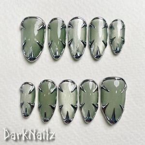 May include: Ten silver-rimmed, green-toned, oval-shaped press-on nails with a cross-hatch design.