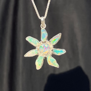 Puede incluir: Un collar de cadena de plata con un colgante en forma de flor hecho de piedras de ópalo iridiscentes.
