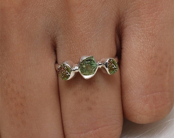 May include: A silver ring featuring three green and brown gemstones. The gemstones are set in a bezel setting and are arranged in a row.
