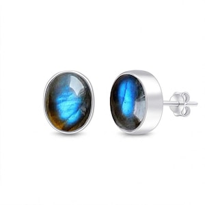 Puede incluir: Un par de pendientes de plata con piedras de labradorita ovaladas. Las piedras muestran una iridiscencia azul y dorada, engastadas en un bisel de plata pulida. Los pendientes tienen un cierre de mariposa clásico.