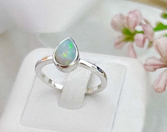 Könnte beinhalten: Ein silberner Ring mit einem tropfenförmigen Opal-Edelstein. Der Opal ist hellblau mit grünen und roten Schimmern.