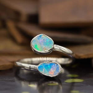 May include: A silver ring with two opal stones set in a twisted band. The opals are a light blue and green colour with a white base.