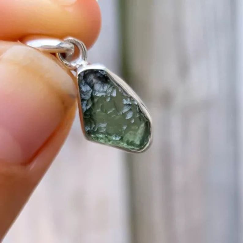 Op de afbeelding: Een zilveren hanger met een ruwe, groene en heldere edelsteen. De edelsteen heeft een ruwe, natuurlijke textuur.