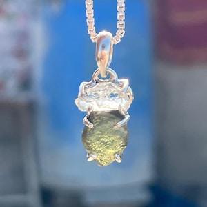 May include: A silver chain necklace with a green gemstone pendant. The gemstone is set in a silver bezel and has a rough, natural texture.