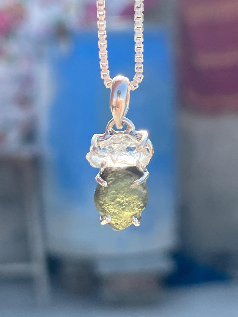 May include: A silver chain necklace with a green gemstone pendant. The gemstone is set in a silver bezel and has a rough, natural texture.