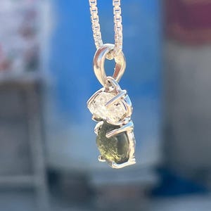 May include: A silver chain necklace with a pendant featuring a green and clear gemstone. The pendant is set in a silver setting and has a delicate design.