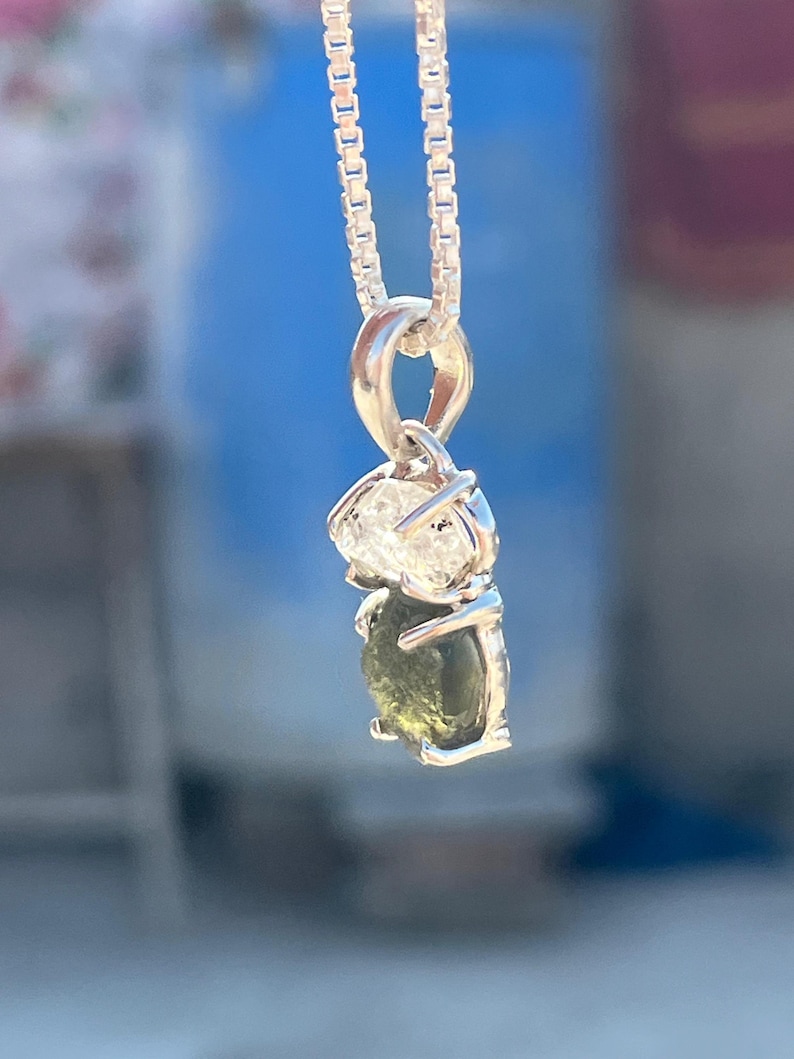 May include: A silver chain necklace with a pendant featuring a green and clear gemstone. The pendant is set in a silver setting and has a delicate design.