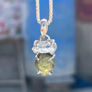May include: A silver chain necklace with a pendant featuring a green gemstone set in a silver bezel. The gemstone is surrounded by a silver halo.