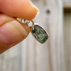 Op de afbeelding: Een zilveren hanger met een ruwe, groene, gefacetteerde edelsteen. De edelsteen is gezet in een zilveren bezel en heeft een ruwe, natuurlijke uitstraling.