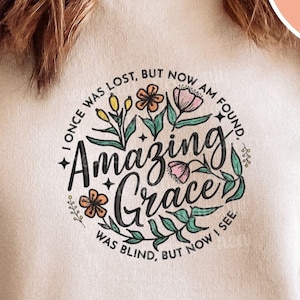 May include: Beige sweatshirt with a round floral design that says "I once was lost, but now am found, Amazing Grace, was blind, but now I see".
