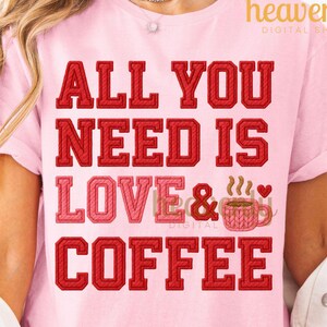 May include: A pale pink t-shirt featuring the slogan "ALL YOU NEED IS LOVE & COFFEE" in red and pink text. The design includes a coffee cup graphic. The shirt has short sleeves.