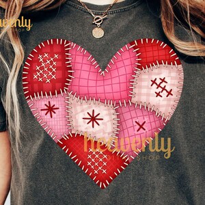 May include: Dark gray t-shirt featuring a patchwork heart design in shades of red and pink. The heart is composed of various stitched fabric pieces. The text "heavenly shop" is printed on the shirt.