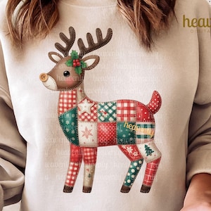Könnte beinhalten: Beiges Sweatshirt mit einem farbenfrohen Patchwork-Rentier-Design. Das Rentier hat braune Geweihe, eine rote Nase und einen Patchwork-Körper mit roten, grünen und weißen Mustern. Der Text "heavenly DIGITAL SHOP" ist oben rechts aufgedruckt.