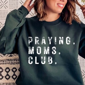 May include: A dark green sweatshirt with the text "Praying Moms Club." printed in white.
