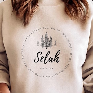 May include: A beige sweatshirt with a black circular design featuring a forest scene, the word "Selah", and the text "Psalm 66:4". The text around the design reads "YOU, AND WILL SING PRAISES TO YOU; THEY WILL SING PRAISES TO YOUR NAME. ALL THE EARTH WILL WORSHIP",