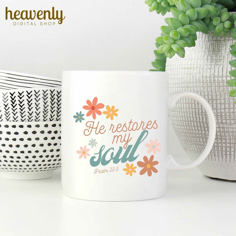 Puede incluir: Taza de cer&aacute;mica blanca con un dise&ntilde;o floral en azul verdoso y naranja. La taza tiene el texto "He restores my soul" y "Psalm 23:3" impreso en ella.