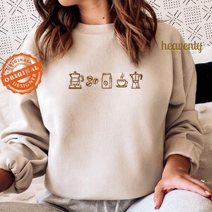 May include: A beige sweatshirt with a brown graphic of coffee beans, a coffee pot, a cup of coffee, and a bag of coffee beans.