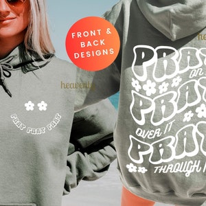 May include: A sage green hoodie with white text and flower graphics. The front features a smiley face design with the words "PRAY PRAY PRAY". The back displays "PRAY on it, PRAY over it, PRAY through it".