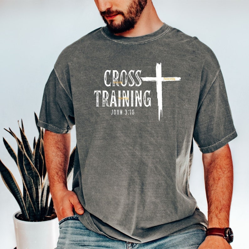 Może przedstawiać: Szary T-shirt z białym krzyżem i napisem "CROSS TRAINING" oraz "JOHN 3:16" w kolorze białym. Krzyż ma napis "heavenly" w kolorze złotym.