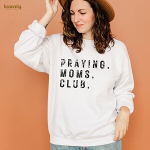 May include: White sweatshirt with black text that reads "Praying. Moms. Club."