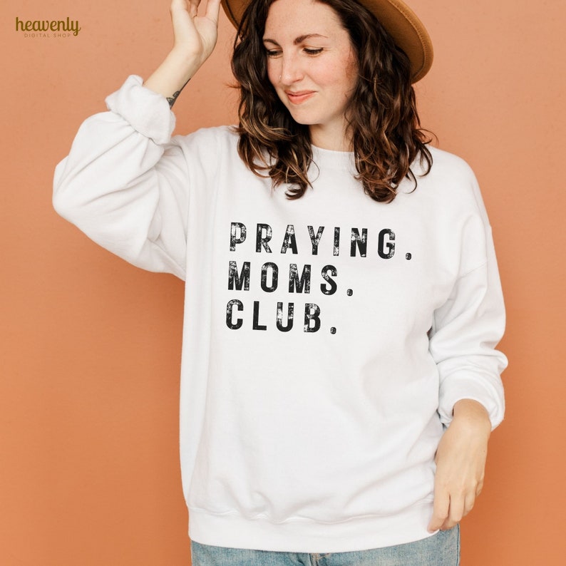 May include: White sweatshirt with black text that reads "Praying. Moms. Club."