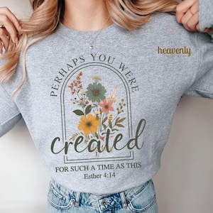 K&ouml;nnte beinhalten: Ein graues Sweatshirt mit dem Text "Perhaps you were created for such a time as this Esther 4:14" in einem schwarzen Bogen mit einem floralen Design im Inneren. Der Text ist in brauner Schrift.