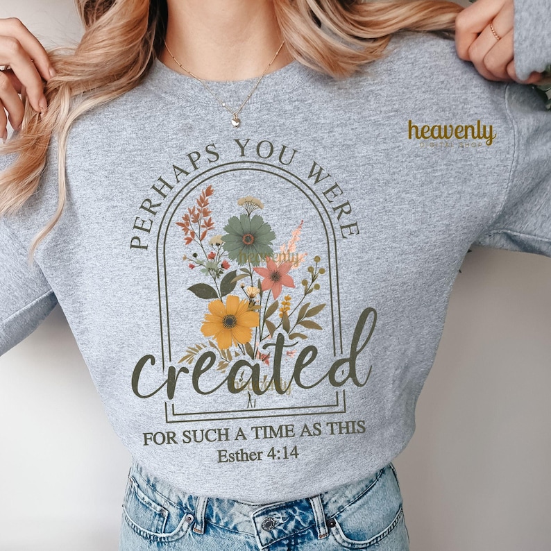 K&ouml;nnte beinhalten: Ein graues Sweatshirt mit dem Text "Perhaps you were created for such a time as this Esther 4:14" in einem schwarzen Bogen mit einem floralen Design im Inneren. Der Text ist in brauner Schrift.