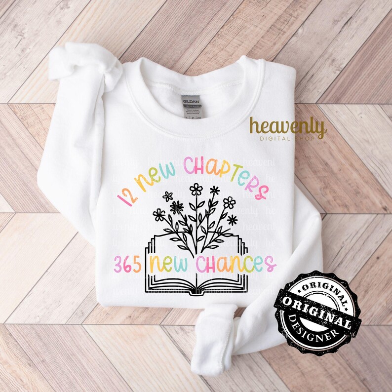 May include: A white sweatshirt with a black graphic design of an open book with flowers and the text "12 new chapters 365 new chances".