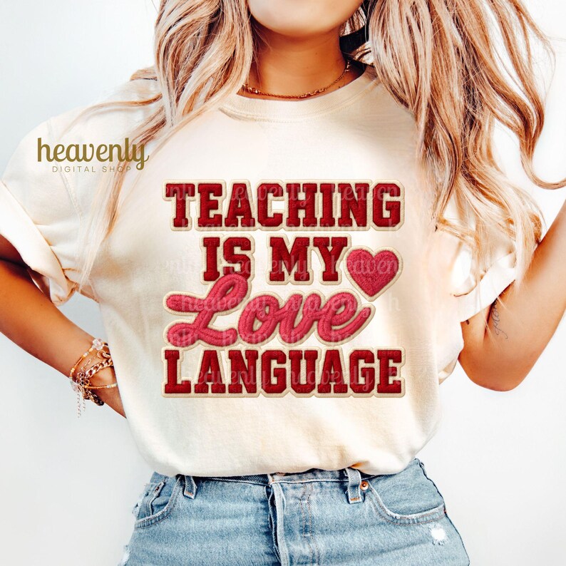 K&ouml;nnte beinhalten: Cremefarbenes T-Shirt mit dem Text "TEACHING IS MY LOVE LANGUAGE" in roter und rosa Schrift. Das Shirt hat eine Herzgrafik und wird mit einer blauen Jeans getragen.