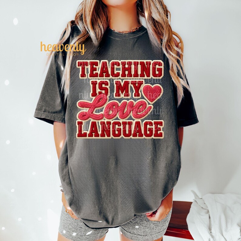 K&ouml;nnte beinhalten: Dunkelgraues T-Shirt mit dem Text "TEACHING IS MY LOVE LANGUAGE" in roter und cremefarbener Schrift. Das Shirt hat kurze &Auml;rmel und eine lockere Passform. Das Design beinhaltet ein Herzsymbol.